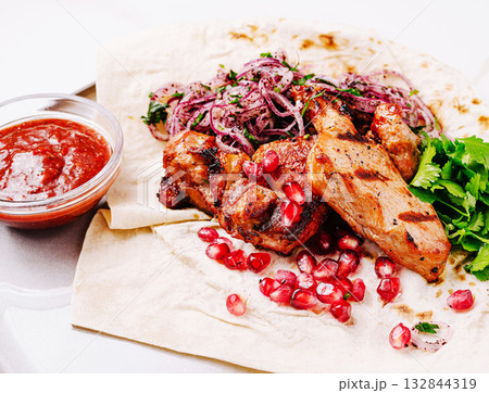 Delicious grilled meat served with pomegranate and fresh herbs on flatbread Delicious grilled meat served with pomegranate and fresh herbs on flatbread 132844319