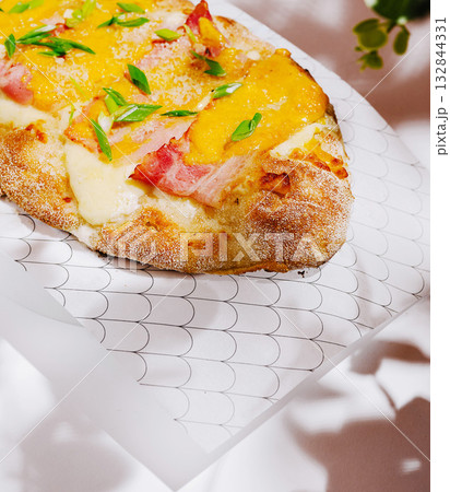 Tasty flatbread topped with cheese and ham served in a cozy setting 132844331