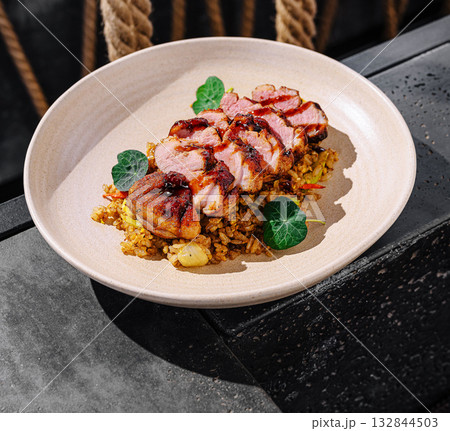 Delicious grilled duck pieces served on a plate with flavorful rice on a table Delicious grilled duck pieces served on a plate with flavorful rice on a table 132844503