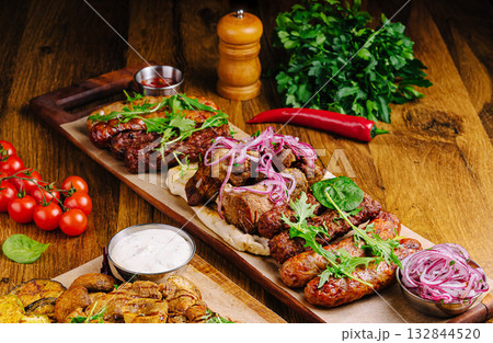 Grilled meats served on a wooden platter with garnishes and sides Grilled meats served on a wooden platter with garnishes and sides 132844520