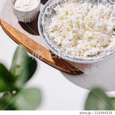 Fresh cottage cheese served in a rustic bowl with cream and greenery 132844528