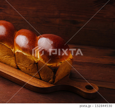 Freshly baked brioche loaf on wooden serving board in warm lighting Freshly baked brioche loaf on wooden serving board in warm lighting 132844530