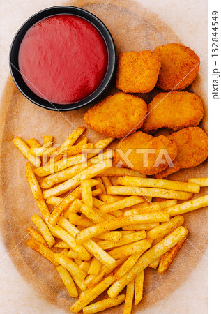 Golden chicken nuggets and crispy fries served with ketchup in a casual setting Golden chicken nuggets and crispy fries served with ketchup in a casual setting 132844549