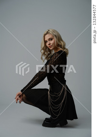 Young woman poses elegantly in a black outfit with chains in a minimal studio setting 132844577