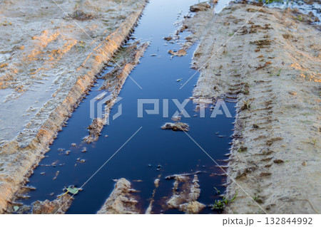 Dark, polluted water collects in a dirt pathway, highlighting the ongoing issue of environmental pollution from waste 132844992