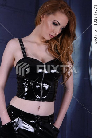 Tall, beautiful, redhead model in black PVC outfits, posing by the window in an old house Tall, beautiful, redhead model in black PVC outfits, posing by the window in an old house 132845078