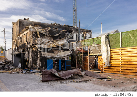 Aerial view of fire damaged building roof and walls collapsed charred facade and debris surround blue generator intact fence and hedge contrast starkly with destruction and cordoned investigation zone Aerial view of fire damaged building roof and walls collapsed charred facade and debris surround blue generator intact fence and hedge contrast starkly with destruction and cordoned investigation zone 132845455