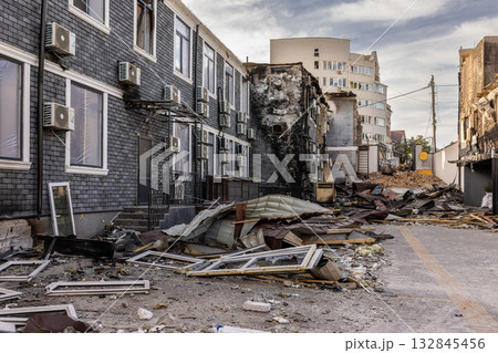 Aerial view of urban destruction partially intact buildings with AC units contrast collapsed fire damaged structure and scattered debris modern tower looms in background amid stark post disaster scene 132845456