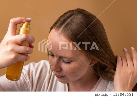 Woman using golden spray bottle for moisturizing hair and scalp 132845551