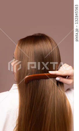 Woman combing long straight hair with wooden brush on neutral background 132845563