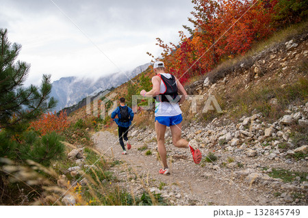 Rear view two male runners with backpacks running mountain autumn marathon 132845749
