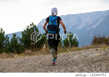 Rear view female athlete with trekking poles in her hands running mountain marathon 132845751