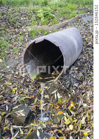 An old iron drain pipe with water leaking out of it An old iron drain pipe with water leaking out of it 132846152