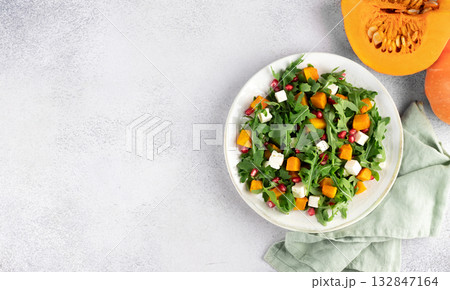Pumpkin salad with arugula, feta cheese, pomegranate seeds on gray background. Top view. Thanksgiving Dishes. Copy space Pumpkin salad with arugula, feta cheese, pomegranate seeds on gray background. Top view. Thanksgiving Dishes. Copy space 132847164