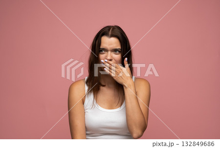 Young woman covering mouth in surprise looking shocked or embarrassed in studio with pink background Young woman covering mouth in surprise looking shocked or embarrassed in studio with pink background 132849686