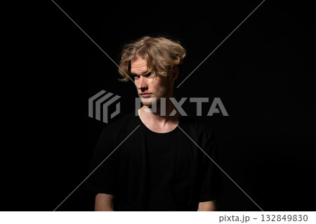 Suspicious man in black shirt looking sideways in low key portrait with dramatic lighting Suspicious man in black shirt looking sideways in low key portrait with dramatic lighting 132849830