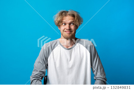 Awkward man in gray and white shirt smiling nervously and looking sideways on blue background Awkward man in gray and white shirt smiling nervously and looking sideways on blue background 132849831