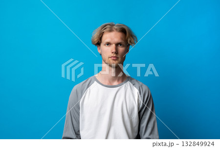 Calm man in gray and white shirt with neutral facial expression on blue background Calm man in gray and white shirt with neutral facial expression on blue background 132849924