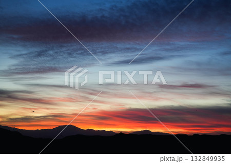 Vivid sunset sky over dark mountain silhouette with colorful clouds and gradient light in evening Vivid sunset sky over dark mountain silhouette with colorful clouds and gradient light in evening 132849935