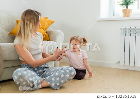 Mother and daughter relaxing together at home on the wooden floor near the sofa. Emotional balance, gentle parenting, and love in a calm domestic environment. 132851019