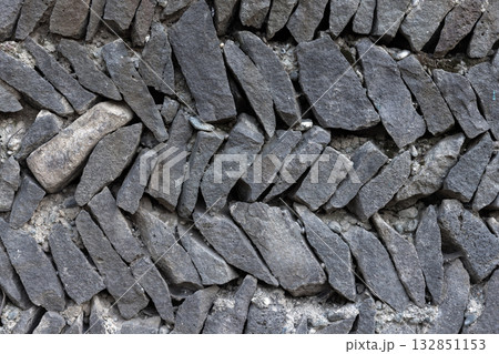 Close-up of a stacked, dry-stone wall built from irregular dark gray rocks. Close-up of a stacked, dry-stone wall built from irregular dark gray rocks. 132851153