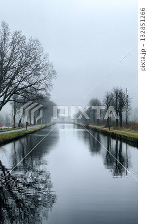 A Misty River Landscape Featuring Reflective Water Surrounded by Bare Trees in Nature A Misty River Landscape Featuring Reflective Water Surrounded by Bare Trees in Nature 132851266
