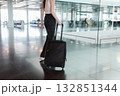 Young woman walking through airport terminal with black suitcase, motion blur. Concept of independent travel, modern lifestyle and seamless mobility. Photo in motion, soft focus. 132851344