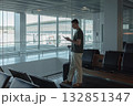 Man stands at a large airport window, holding his suitcase and checking his phone while waiting for his flight. Concept of solitude, anticipation and modern travel technology. 132851347