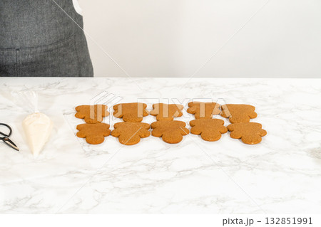 A neat arrangement of gingerbread girl cookies, fully decorated with white royal icing, placed in rows on a marble countertop. 132851991