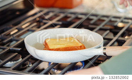 Within the sleek setting of a modern white kitchen, banana slices and brioche bread sizzle on a non-stick pan over a gas stove, setting the stage for an enticing grilled peanut butter banana sandwich. Within the sleek setting of a modern white kitchen, banana slices and brioche bread sizzle on a non-stick pan over a gas stove, setting the stage for an enticing grilled peanut butter banana sandwich. 132852002