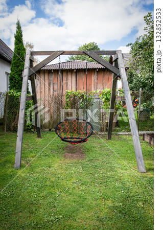 Wooden swing frame with round rope swing in backyard garden setting 132852533