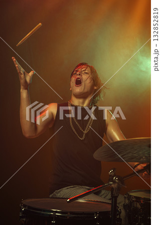 Drummer tossing drumstick in air with expression and warm stage lighting Drummer tossing drumstick in air with expression and warm stage lighting 132852819