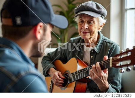 Grandson teaching her grandma how to play the guitar. Retired Senior lady have fun with musical instrument wile sitting on sofa, Hobby and leisure activity. Mental health. Grandson teaching her grandma how to play the guitar. Retired Senior lady have fun with musical instrument wile sitting on sofa, Hobby and leisure activity. Mental health. 132853529