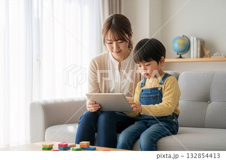 母子が1台のタブレットを並んで笑顔で見ているシーン 母子が1台のタブレットを並んで笑顔で見ているシーン 132854413