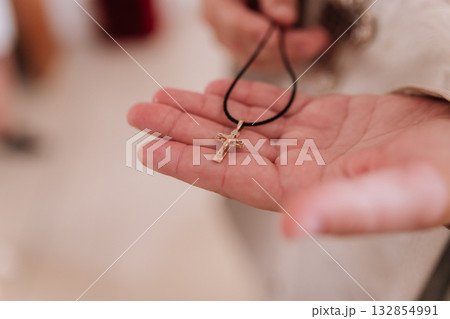 Priest hand holding golden cross pendant on black cord, baptism faith symbol 132854991