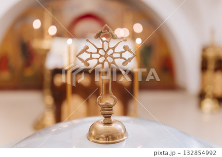 Golden Orthodox cross on baptismal font with soft altar lights, spiritual ceremony Golden Orthodox cross on baptismal font with soft altar lights, spiritual ceremony 132854992