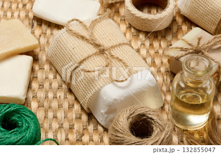 Natural handmade soap bars with various craft supplies on a woven mat. The soap bars are wrapped in burlap and twine. Natural handmade soap bars with various craft supplies on a woven mat. The soap bars are wrapped in burlap and twine. 132855047