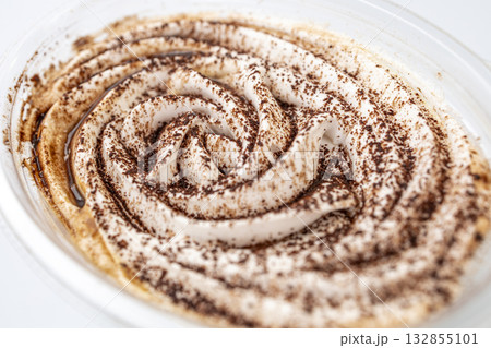 Close up of banoffee dessert in plastic cup, featuring swirl of whipped cream dusted with cocoa powder, resembling a fingerprint 132855101