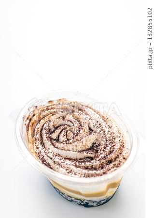 Delicious banoffee dessert in plastic cup, featuring layers of banana, toffee, and cream, topped with cocoa powder on white 132855102