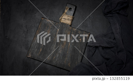 A vintage black cutting board with a handle tied with twine and dark cheesecloth on a black textured background. A vintage black cutting board with a handle tied with twine and dark cheesecloth on a black textured background. 132855119