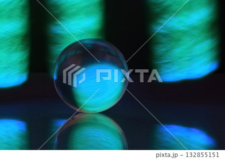 Glowing Orb Reflections. A glowing glass orb set against a backdrop of vibrant blue and green light. Glowing Orb Reflections. A glowing glass orb set against a backdrop of vibrant blue and green light. 132855151