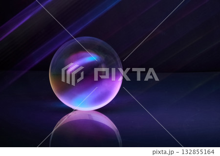 Luminous Sphere. A glowing orb reflects vibrant purple and blue hues on a shiny surface 132855164