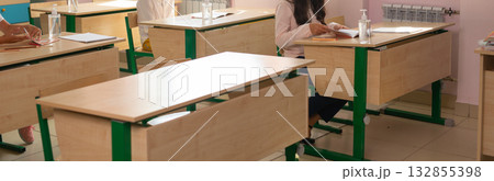 Several students sitting at separate desks during classroom activity, banner. Education, distance learning, and modern safety in academic environment. 132855398