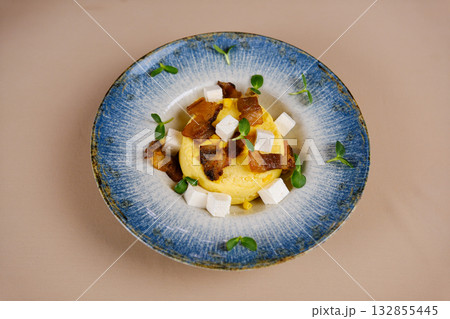 corn porridge with bacon Banush or banosh is Ukrainian dish prepared from cornmeal with cream topped with bacon, onion and bryndza closeup on the bowl on the wooden table. Vertical top view from above corn porridge with bacon Banush or banosh is Ukrainian dish prepared from cornmeal with cream topped with bacon, onion and bryndza closeup on the bowl on the wooden table. Vertical top view from above 132855445