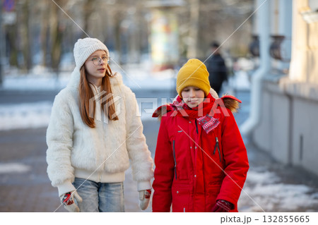 Teenagers in warm clothes walk along the winter streets of the city. Teenagers in warm clothes walk along the winter streets of the city. 132855665