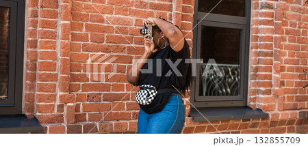 African, american woman photographing building with vintage camera outdoors. Banner with copy space. Exploration, creative process, and visual storytelling in city atmosphere. African, american woman photographing building with vintage camera outdoors. Banner with copy space. Exploration, creative process, and visual storytelling in city atmosphere. 132855709