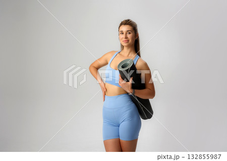 Yoga practitioner poses confidently with a mat, showcasing fitness and health lifestyle in a studio setting Yoga practitioner poses confidently with a mat, showcasing fitness and health lifestyle in a studio setting 132855987
