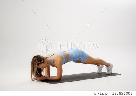 Fitness enthusiast performs plank exercise on yoga mat in bright studio environment Fitness enthusiast performs plank exercise on yoga mat in bright studio environment 132856003