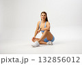 Fit woman sitting gracefully in activewear, showcasing strength and style during a fitness photoshoot in a minimalist studio setting 132856012