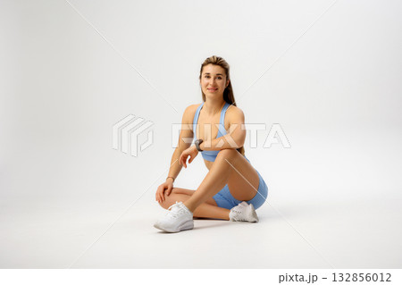 Fit woman sitting gracefully in activewear, showcasing strength and style during a fitness photoshoot in a minimalist studio setting Fit woman sitting gracefully in activewear, showcasing strength and style during a fitness photoshoot in a minimalist studio setting 132856012
